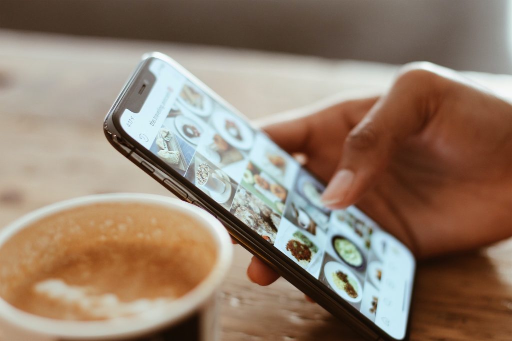 A hand scrolling through the feed of an Instagram profile containing food pictures. Also, there is a coffee cup on the background.